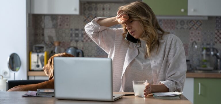 Donna stanca poggiata sulla scrivania con tazza vuota — stanchezza cronica e mancanza di energia